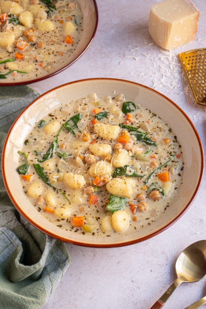 A large brown bowl with creamy vegetarian gnocchi soup with spinach, carrots, and celery.