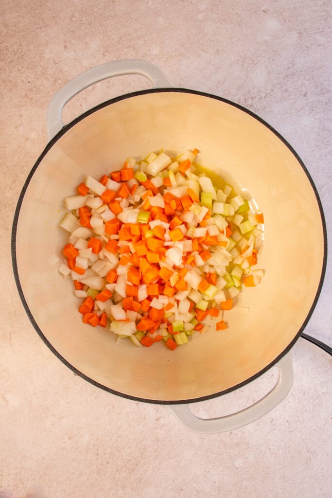 A large dutch oven with diced carrots, onions, and celery inside.