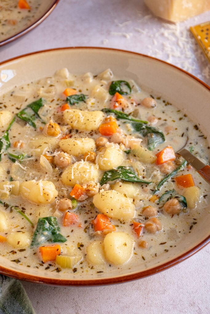 Close up of a bowl of healthy chickpea gnocchi soup with carrots, and spinach.