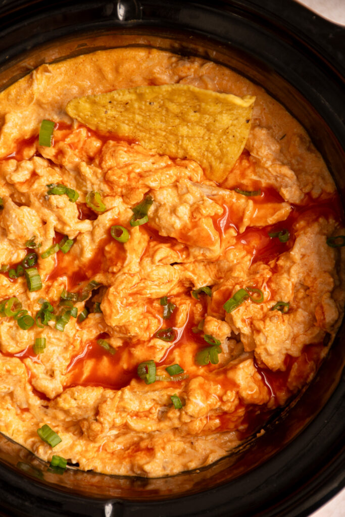 Creamy buffalo chicken dip in a crock pot garnished with hot sauce and green onions.