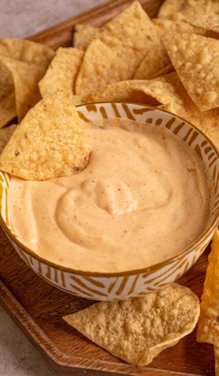 A small bowl with cottage cheese queso with a chip dipped in and tortilla chips surrounding it.