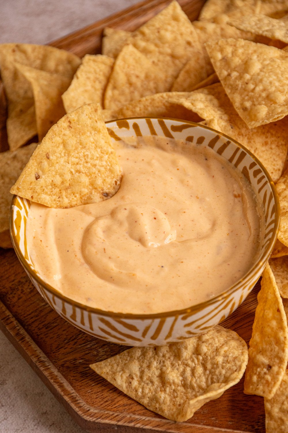 A small bowl with cottage cheese queso with a chip dipped in and tortilla chips surrounding it.