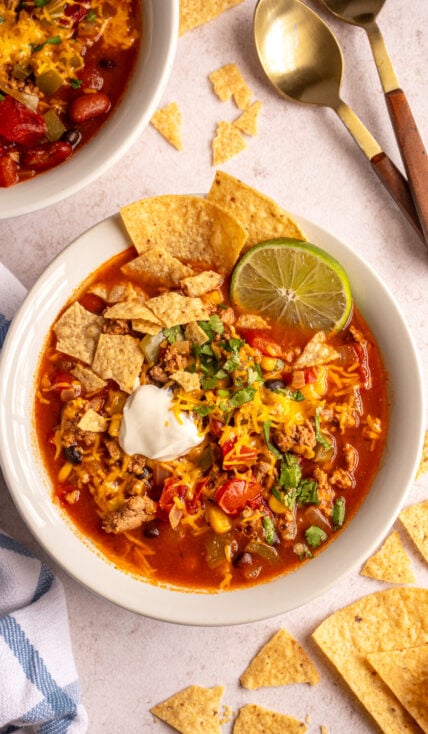 Overhead of a white bowl filled with ground turkey taco soup garnished with shredded cheese, dour cream, cilantro, and tortilla chips.