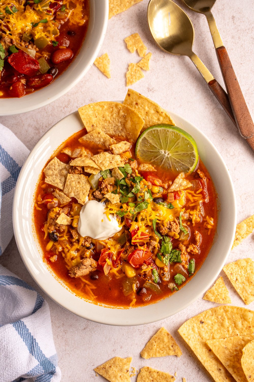 Overhead of a white bowl filled with ground turkey taco soup garnished with shredded cheese, dour cream, cilantro, and tortilla chips.