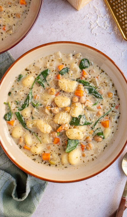 Overhread view of a large brown bowl filled with creamy vegetarian chickpea gnocchi soup with carrots and spinach.