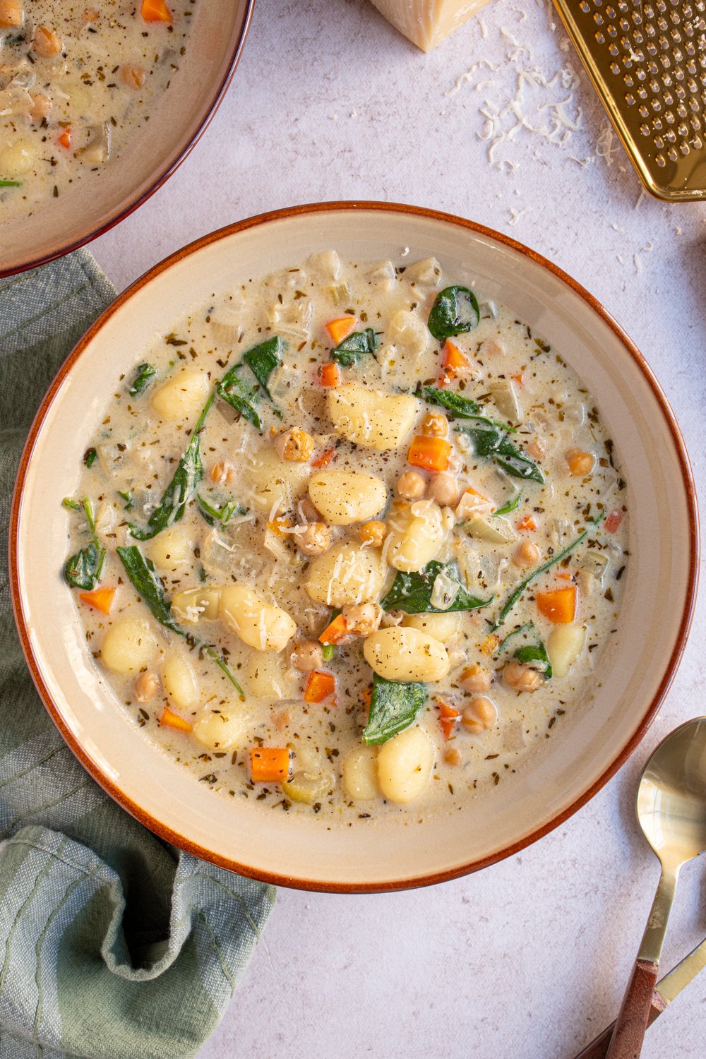 Overhread view of a large brown bowl filled with creamy vegetarian chickpea gnocchi soup with carrots and spinach.