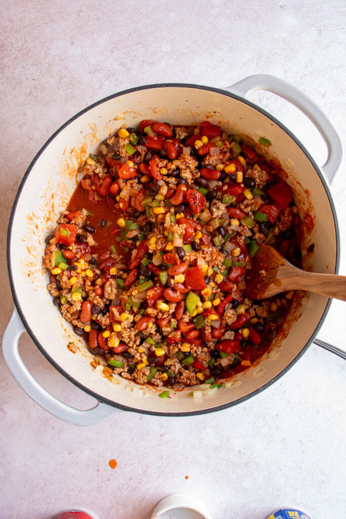 A large pot with all of the ingredient except broth for making turkey taco soup.