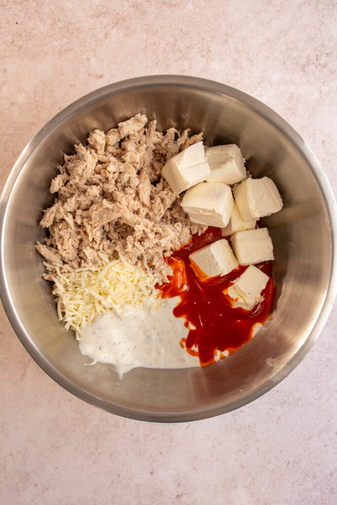 Ingredients for crock pot buffalo chicken dip in a mixing bowl.