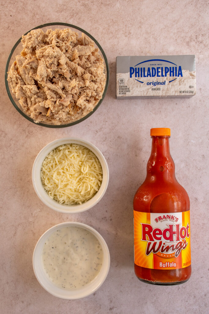 Ingredients to make slow cooker buffalo chicken dip laid out on a tabletop.