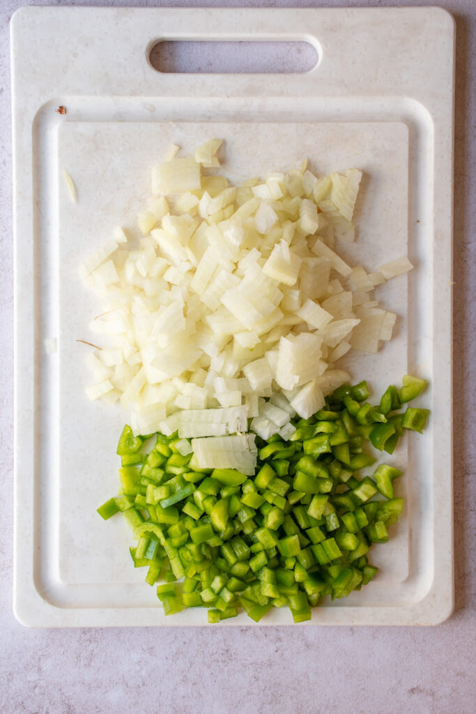 A cutting board with diced green bell peppers and diced onions.