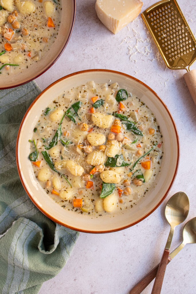 Overhead view of a large brown bowl filled with creamy vegetarian soup with gnocchi, carrots, celery, chickpeas, and spinach.