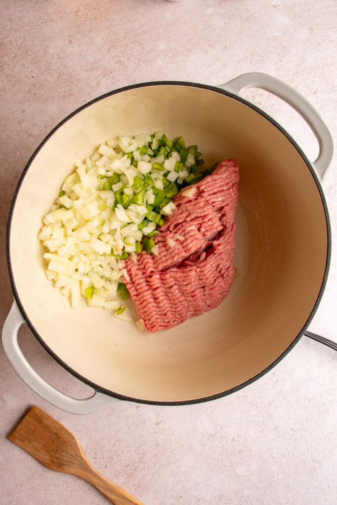 A large pot with ground turkey, diced bell pepper, and diced onion.