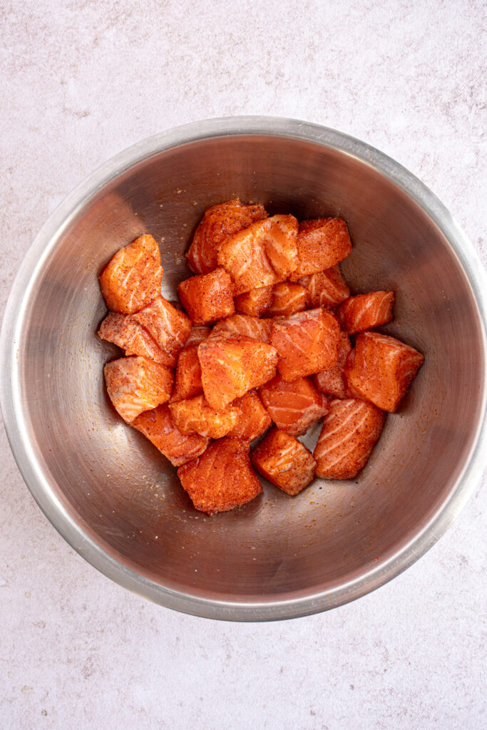 A stainless steel bowl with bite size salmon covered in seasoning.