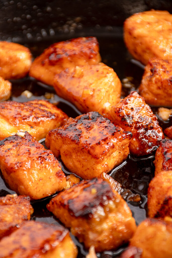 A close up of honey garlic salmon bites in a black cast iron pan.
