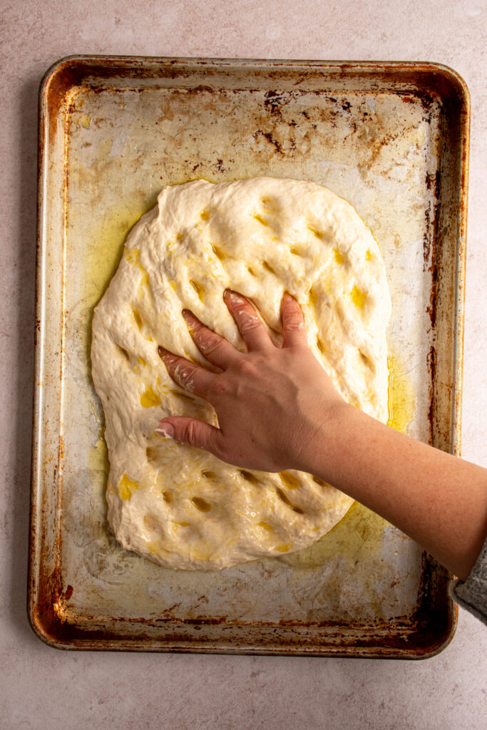 Fingers add dimples to the focaccia bread dough.