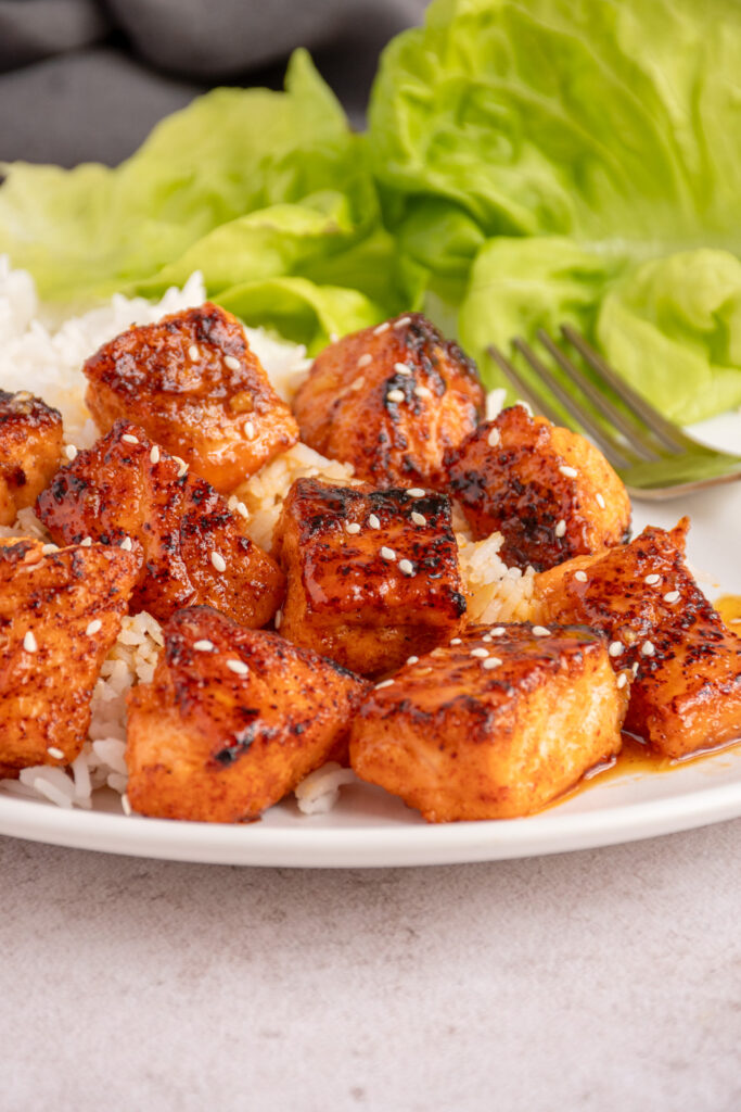 A plate with honey garlic salmon bite on top of a bed or white rice.