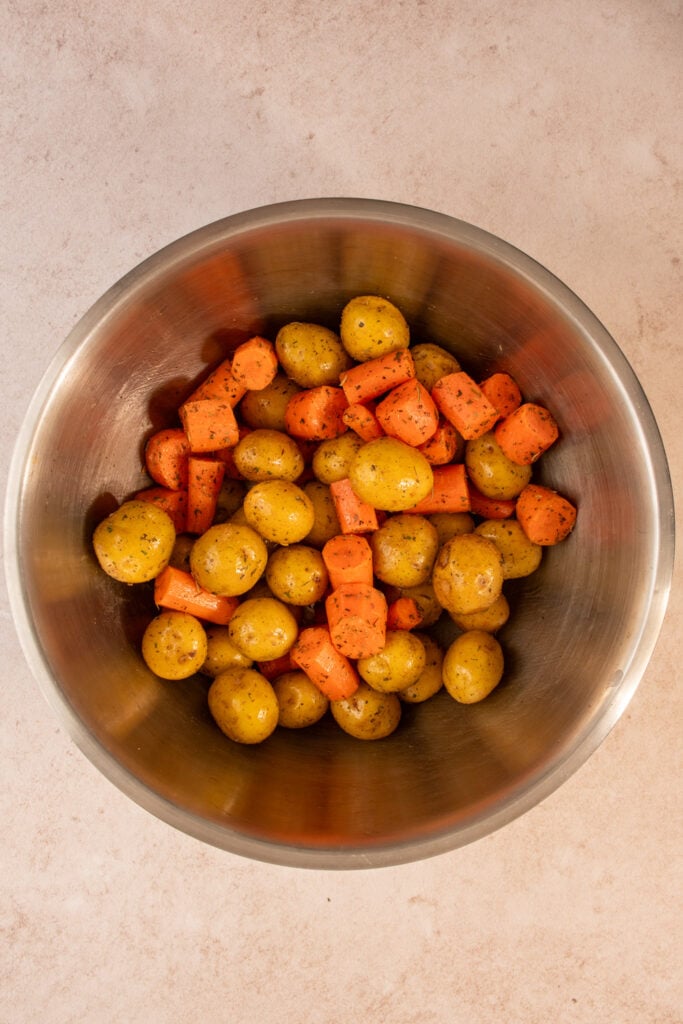 Prepping the carrots and baby potatoes in a mixing bowl with italian seasoning.