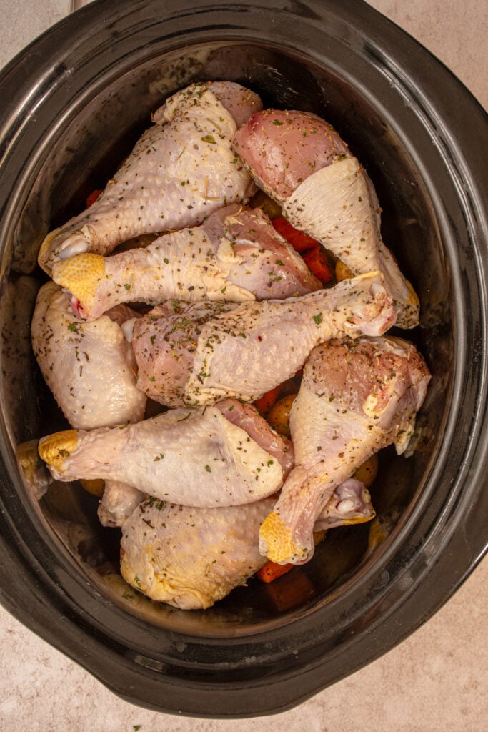 The raw chicken legs on top of the vegetables ready to be cooked.