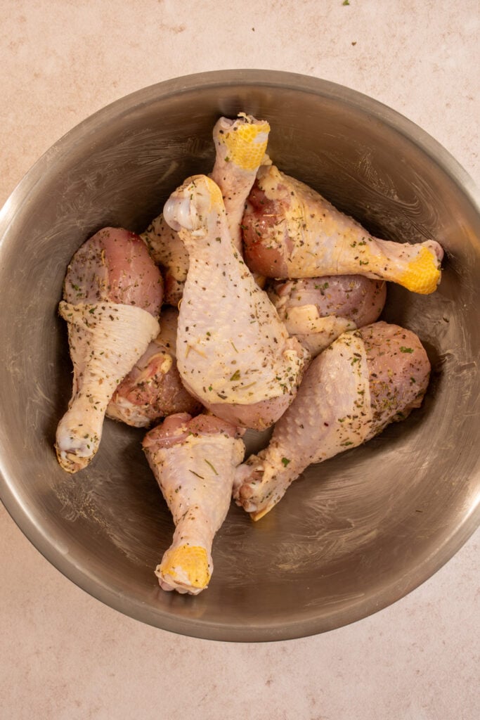 Seasoned chicken legs in a mixing bowl.