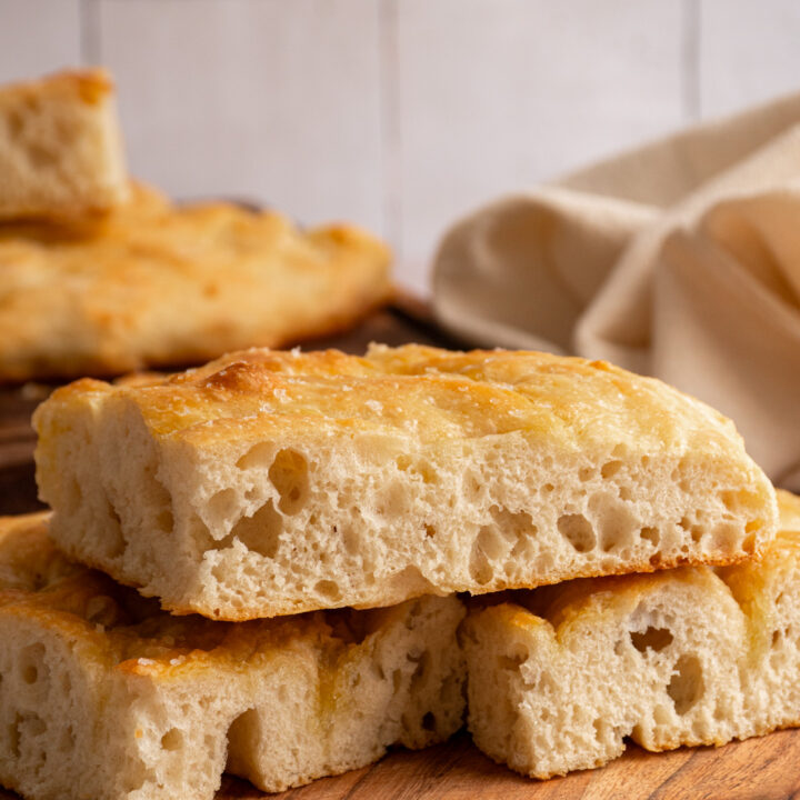Slices of focaccia bread on a wooden plate showing off the airy dough.