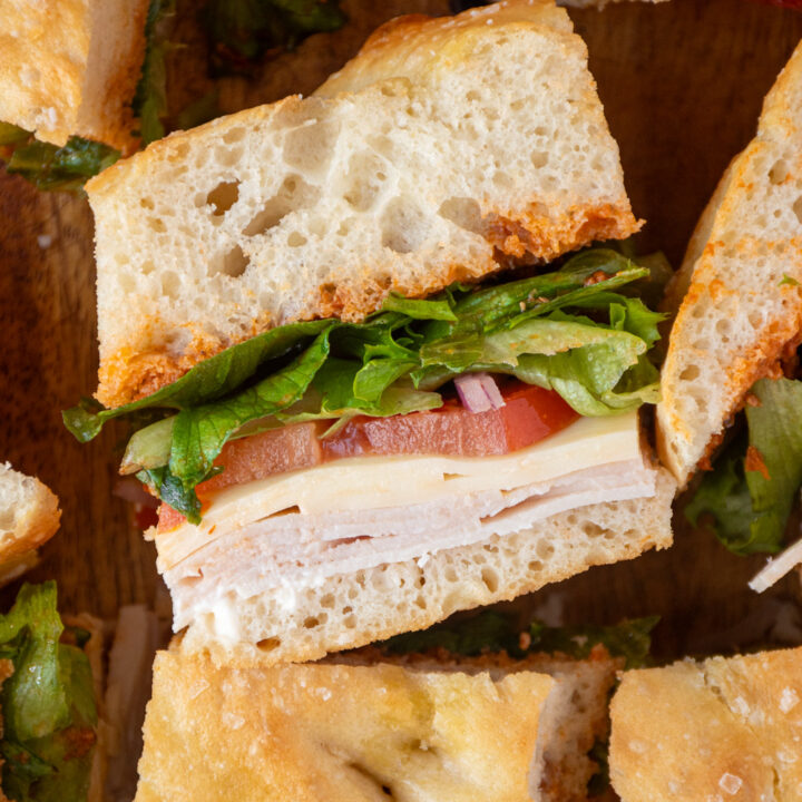 A piece of focaccia turkey sandwich showing layers of turkey, cheese, tomato, lettuce, and sun-dried tomato pesto between focaccia bread.