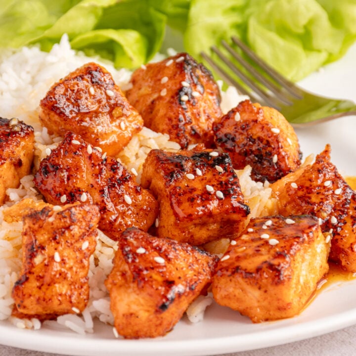 Plate with rice, lettuce, and a serving of honey garlic salmon bites covered in a glaze of honey.