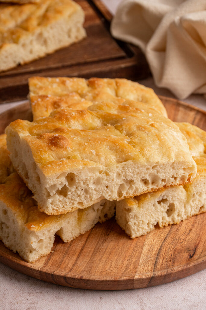 Sliced focaccia bread layered on a wooden plate.