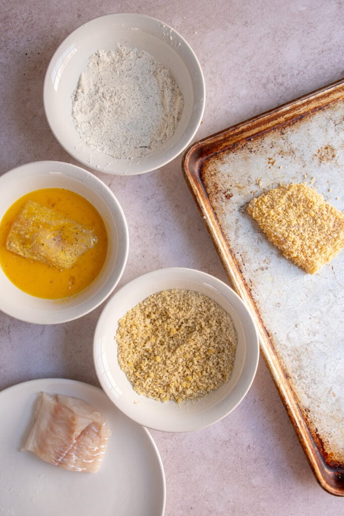 Adding the flour coasted fish fillet to the mixture mixture in a bowl to coat it as part of the breading mixture.