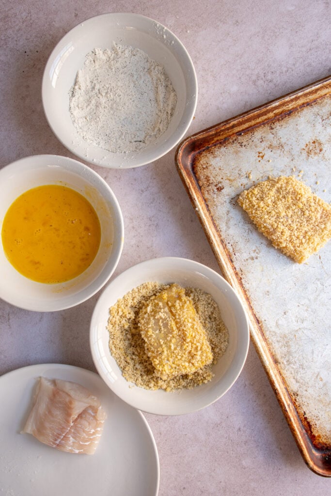 A fish fillet in a bowl of panko breadcrumbs to make a crispy breading on the outside of the baked cod.