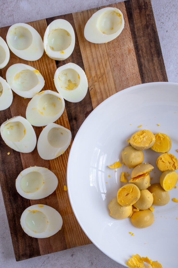 A cutting board with egg white halves and a bowl with egg yolks.