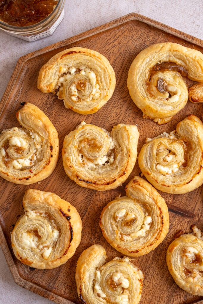 A wood serving tray on a table filled with Fig and Goat Cheese Puff Pastry Pinwheels.
