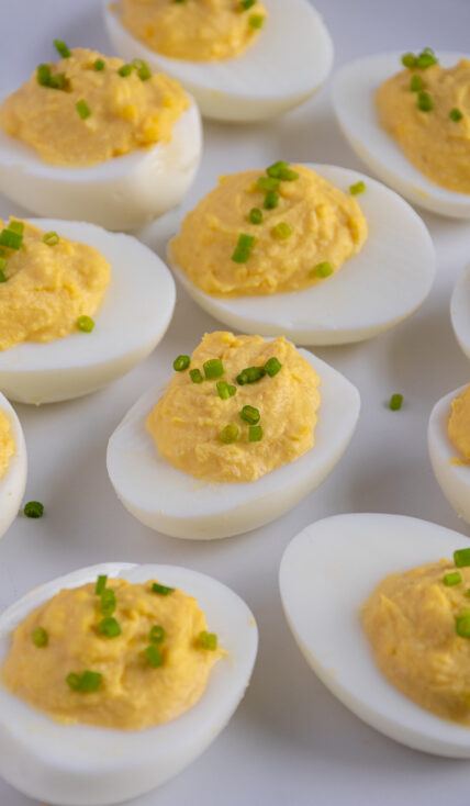 A white plate full of Horseradish Deviled Eggs garnished with fresh chives.