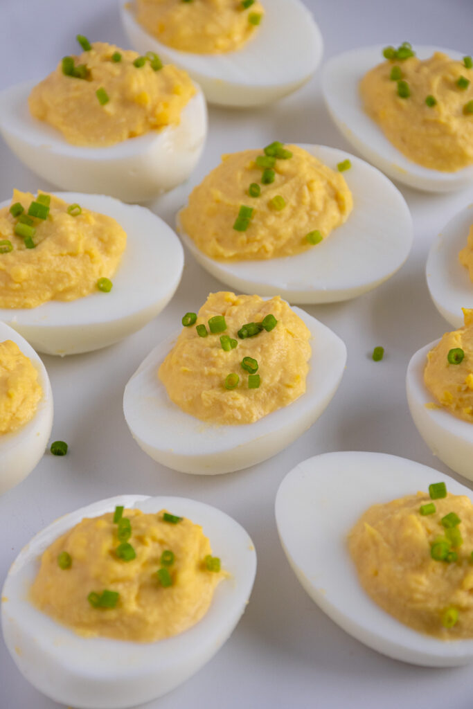 A white plate full of Horseradish Deviled Eggs garnished with fresh chives.