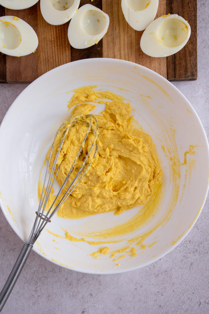 Mixing yolk mixture together in a white bowl with a whisk.