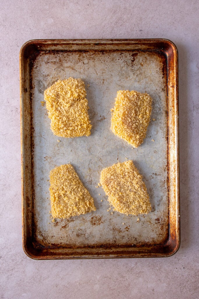 A sheet pan with the raw breaded fish fillets.