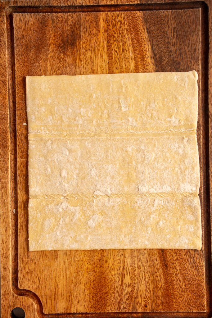 A sheet of puff pastry laid out on a wooden cutting board.