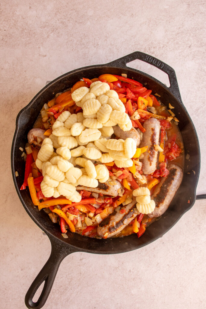 Adding gnocchi to the skillet with the sausages and peppers.