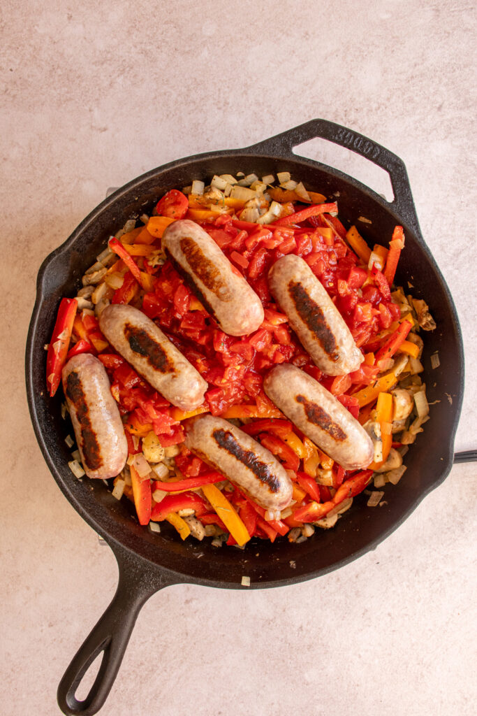 Adding the diced tomatoes and sausages to the skillet.