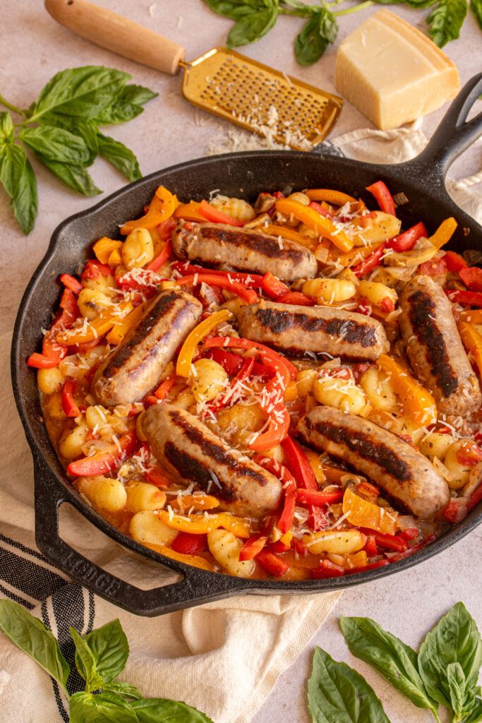 A cast iron skillet filled with colorful peppers, gnocchi, and sausages.
