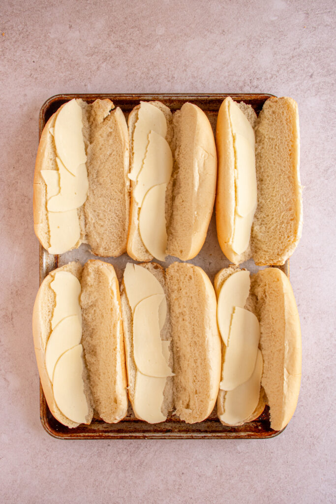 A sheet pan with sub rolls and provolone cheese.
