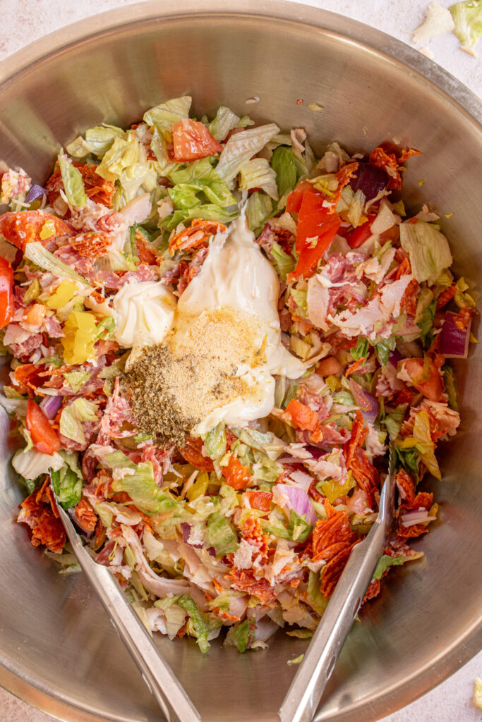 A large bowl with the chopped ingredients and mayo and dressing ingredients for making Chopped Italian Sandwiches.