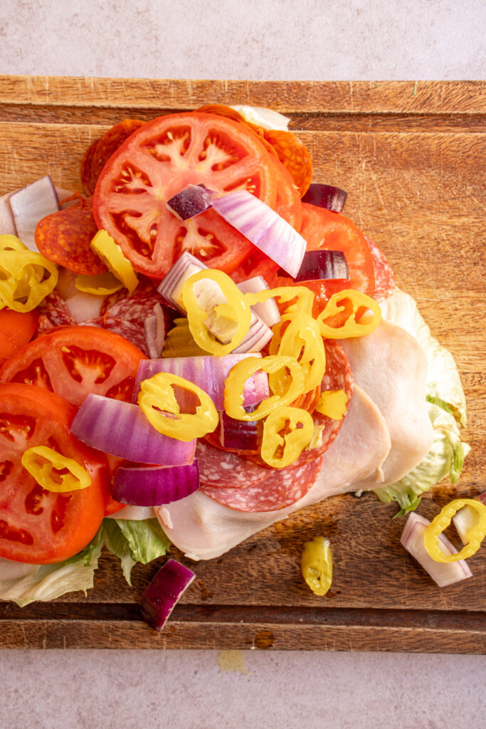 Ingredients ready to be chopped on a wood cutting board to make Chopped Italian Sandwiches.