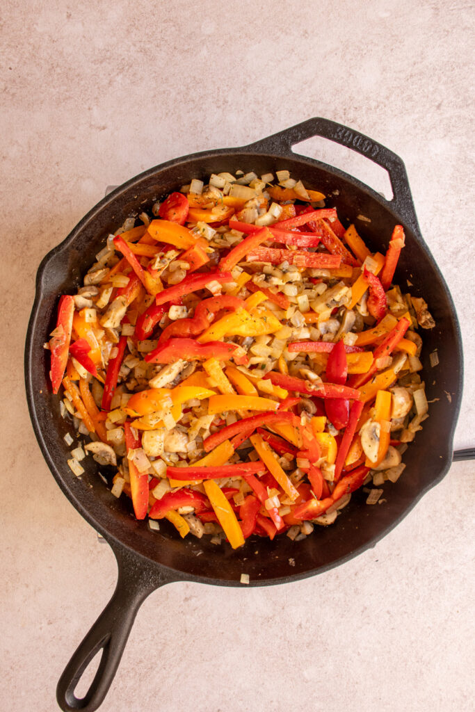 Cooking red and yellow bell peppers in a skillet with onions and mushrooms.