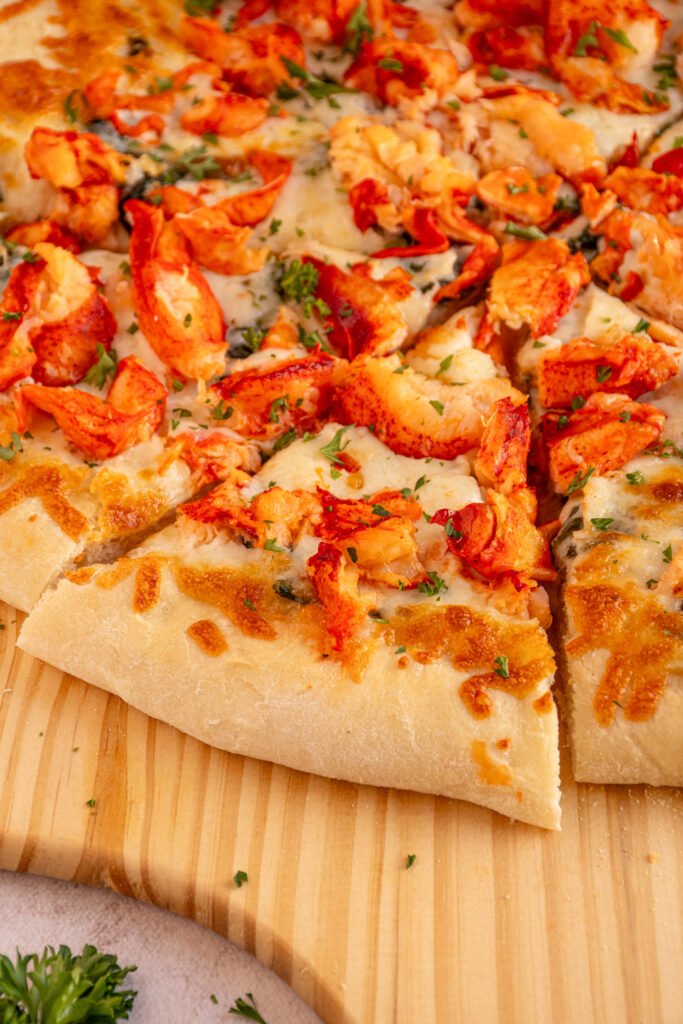 A piece of cut lobster pizza with large chunks of lobster and melty cheese.