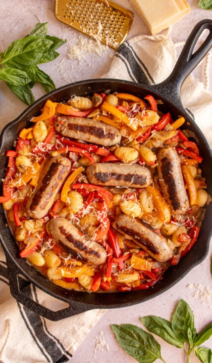 A large cast iron skillet filled with colorful bell peppers, gnocchi, and italian sausages.