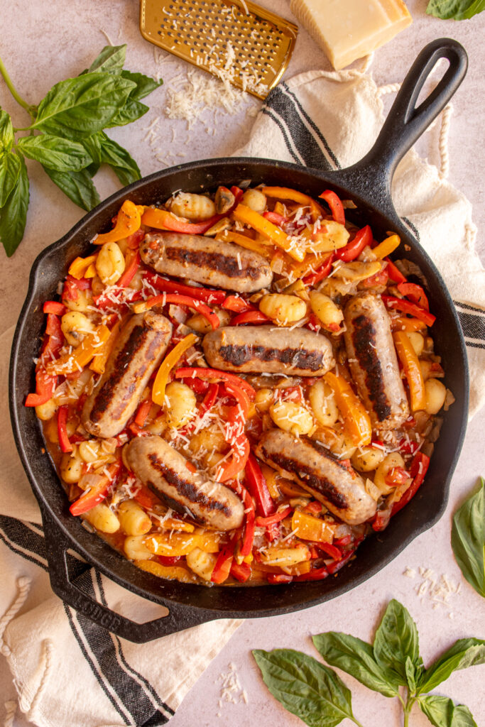 A large cast iron skillet filled with colorful bell peppers, gnocchi, and italian sausages.