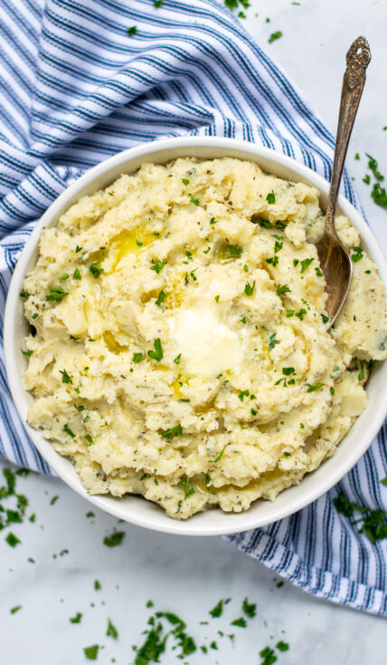 A bowl with herbed mashed potatoes with melted butter on top.