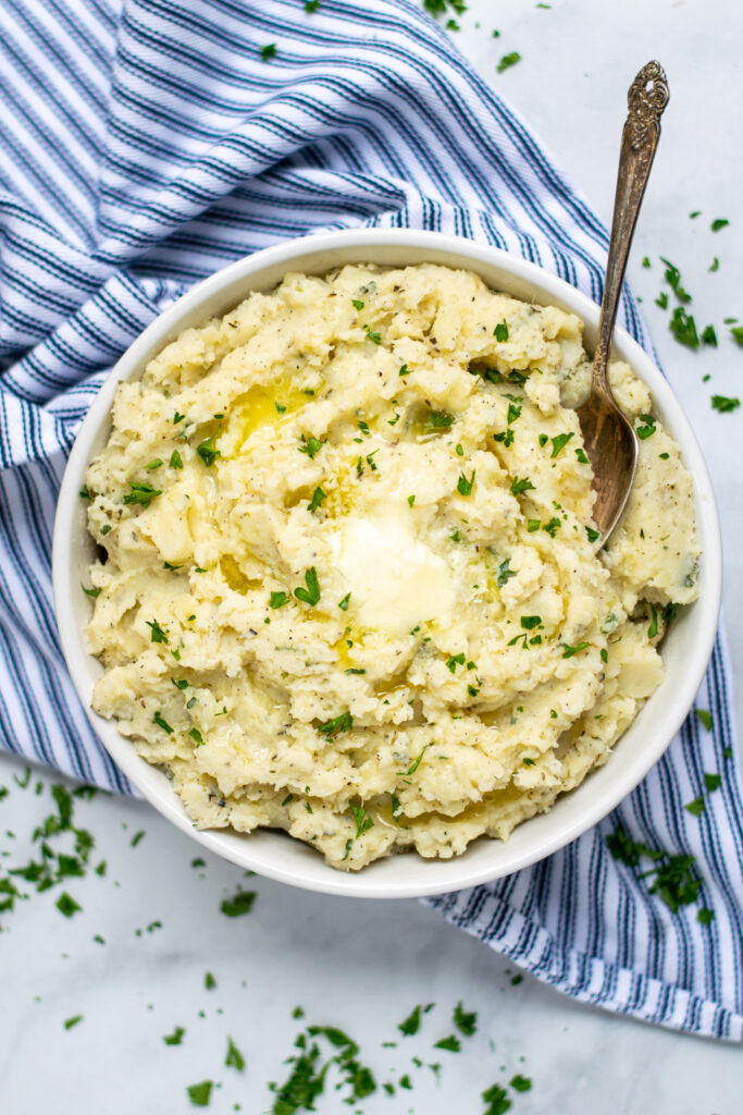 A large bowl filled with herbed mashed potatoes with melted butter and a spoon.