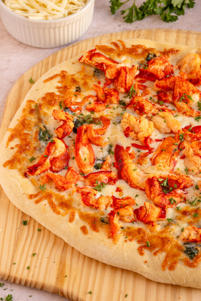 A lobster pizza on a wooden pizza peel with large chunks of lobster.