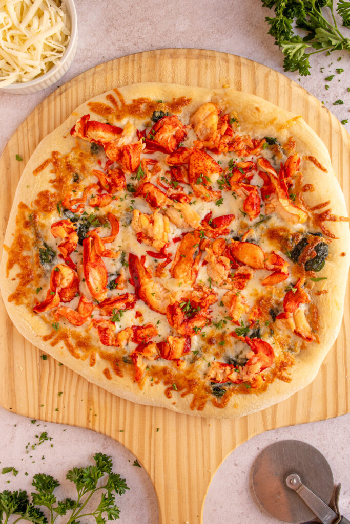 Overhead view of a lobster pizza fresh out of the oven on a pizza peel.